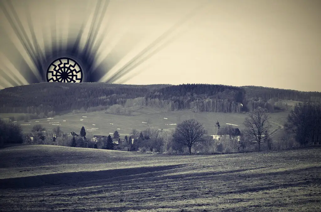 Umělecká fotografie temného symbolu Černého slunce vycházejícího nad českou krajinou s kostelem jako memento nacistického mysticismu.