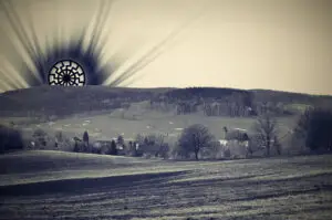 Umělecká fotografie temného symbolu Černého slunce vycházejícího nad českou krajinou s kostelem jako memento nacistického mysticismu.