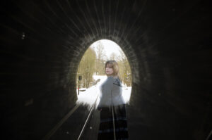 Fotografie ženy stojící v šeru železničního tunelu, dívající se zpět ke světlu na konci. Metafora vnitřní samoty a hledání blízkosti.