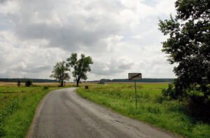 enkovská krajina v srpnu, vinoucí se silnice mezi poli a stromy, s dopravní značkou "Záboří" na kraji, pod zamračenou oblohou, zachycující atmosféru lidových pranostik o počasí.